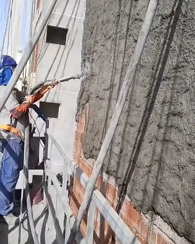 Operador no balancim projetando reboco na fachada do prédio